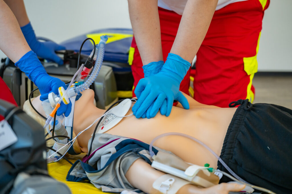 Nahaufnahme einer Reanimationsübung mit Beatmungsgerät, Defibrillator-Pads und Herzdruckmassage.
