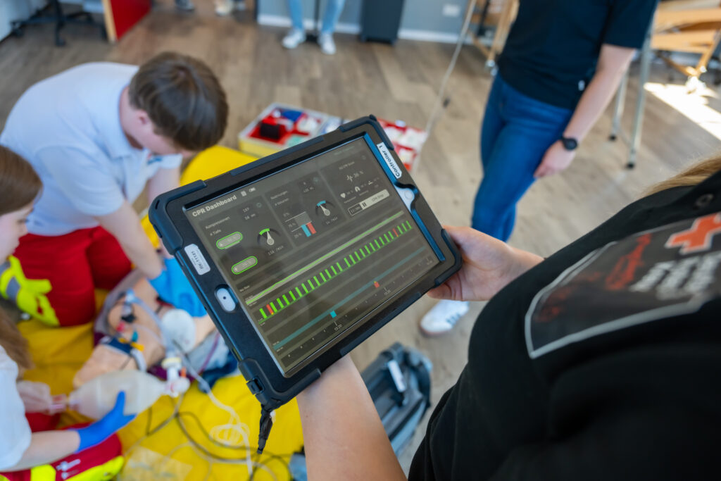 Ausbilderin überwacht eine Reanimationsübung auf einem Tablet mit Echtzeitdaten zur Herzdruckmassage.