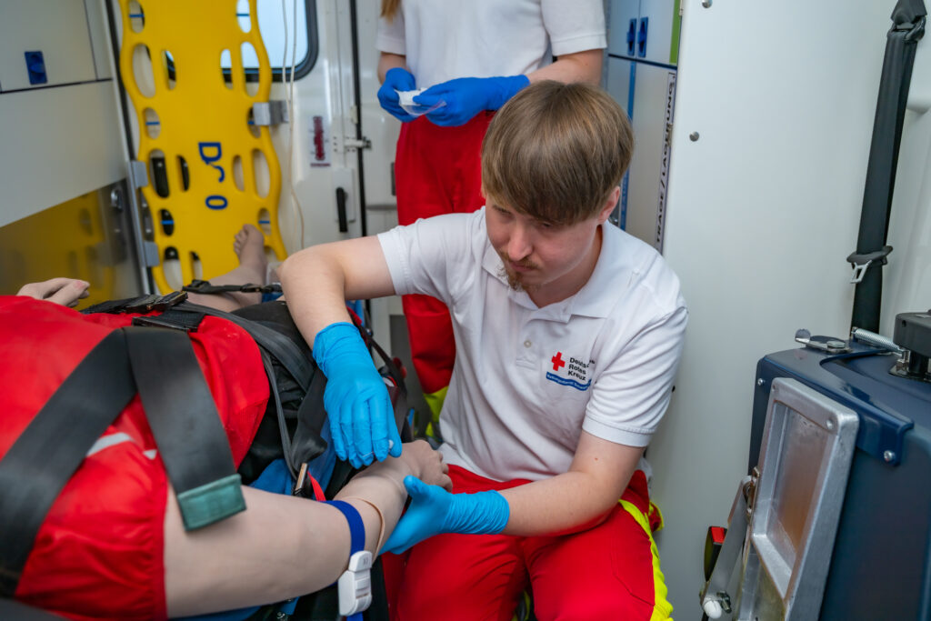 Teilnehmer versorgt während einer Übung eine angeschnallte Patientenpuppe im Rettungswagen.