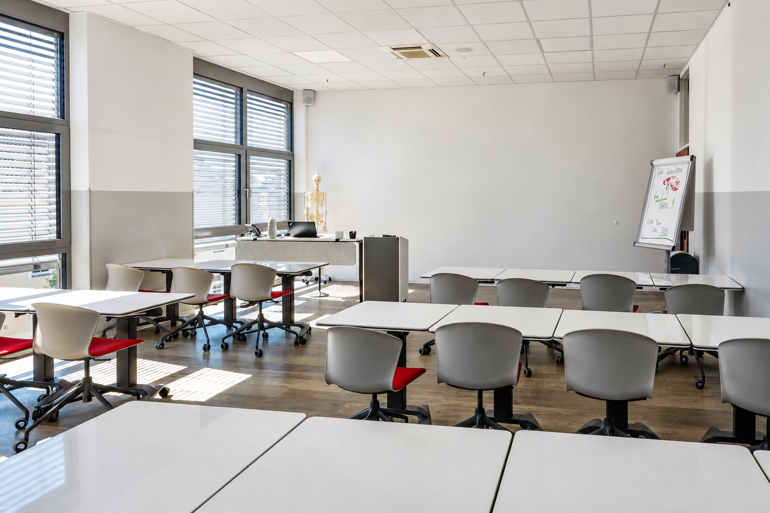 Heller Klassenraum der Rettungsdienstschule mit weißen Tischen, Stühlen und Flipchart.