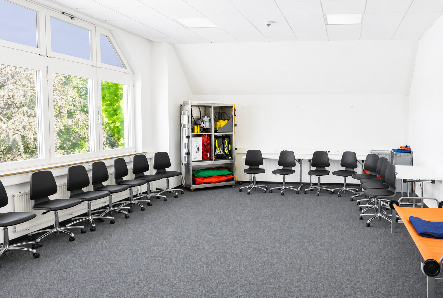 Heller Übungsraum der Rettungsdienstschule mit Stühlen, medizinischer Ausrüstung und Behandlungsliege.